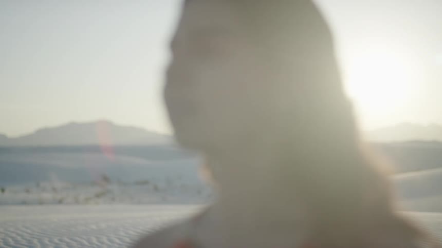 Brunette woman wearing a red dress looks around in the desert at sunset