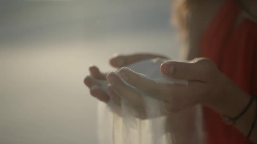A kneeling woman scoops up a handful of white sand in a desert