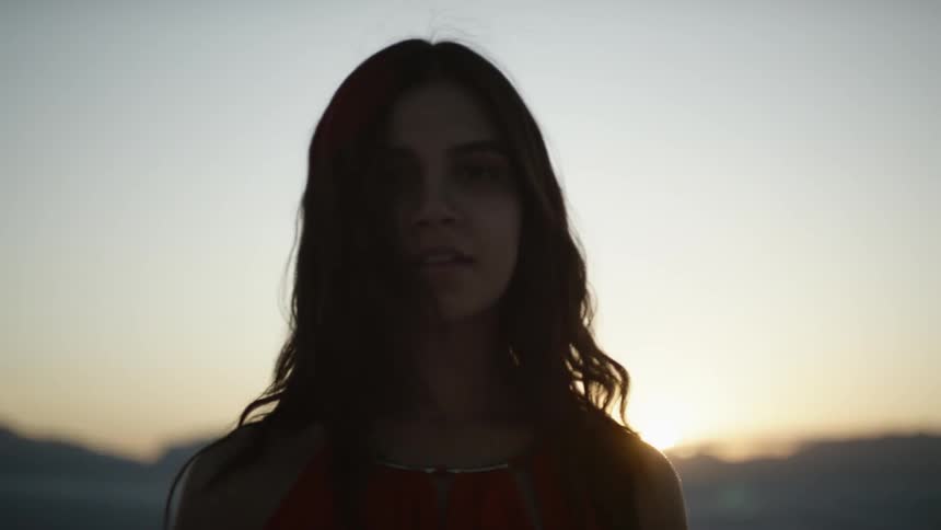 Brunette woman wearing a red dress looks around in the desert at sunset