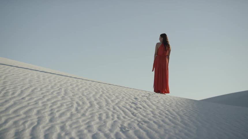 A woman in a long dress walks alone in a sandy desert