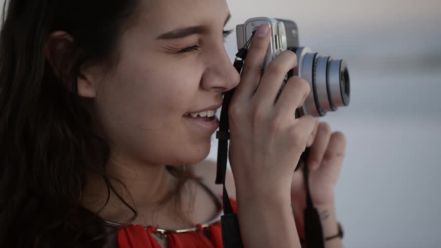 A woman takes a picture with a silver camera outside