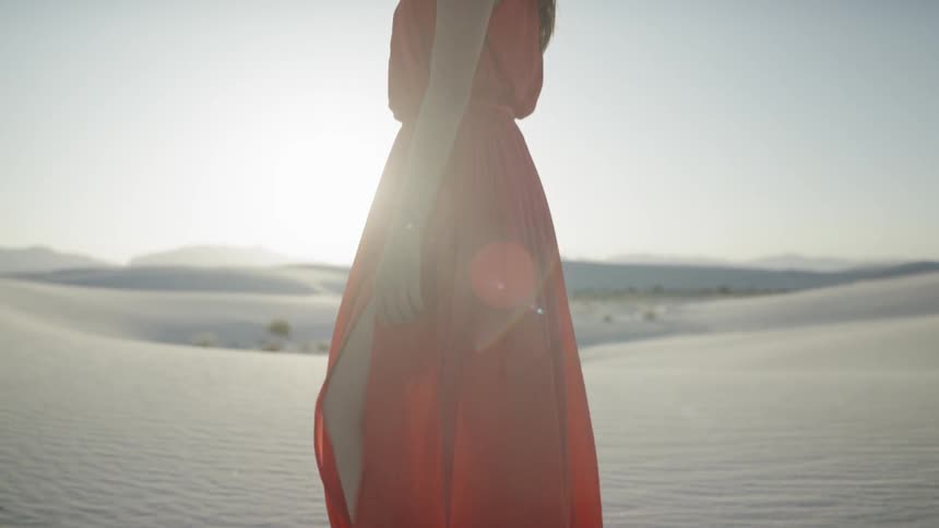 A woman walks barefoot through the sand during sunrise
