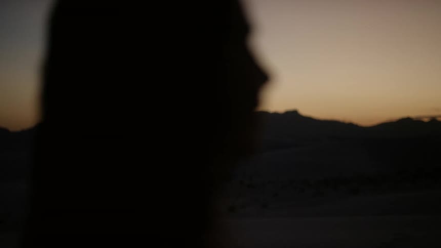 The outline of a woman looking out to the horizon at sunset