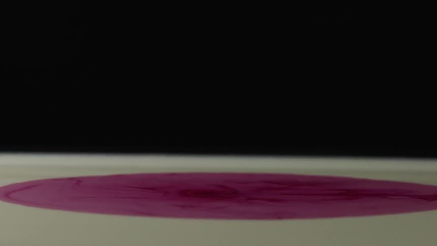A purple droplet is falling and mixing with yellow paint