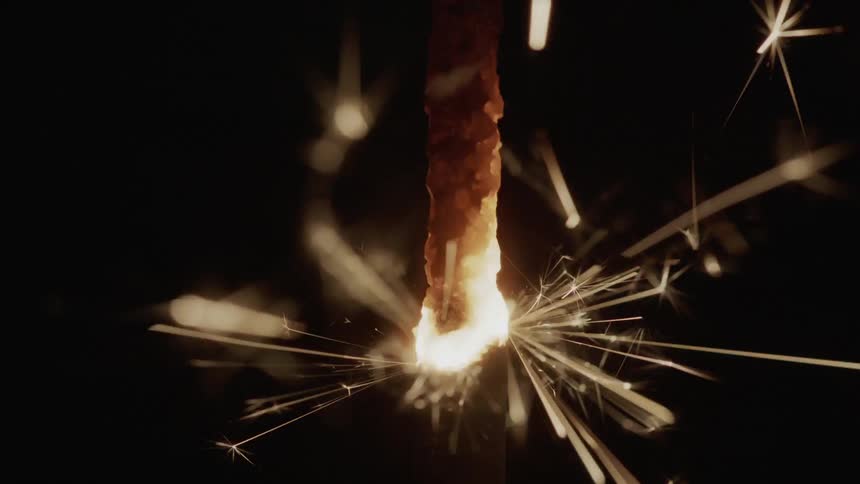 The wick of a sparkling candle is alight and countless sparks are ejecting outward from it