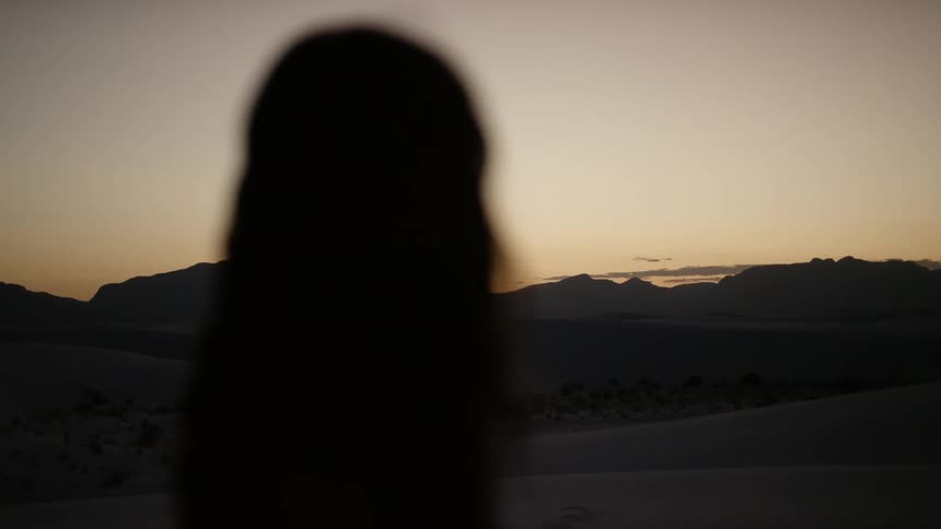 The silhouette of a woman looking at the desert dunes at sunset