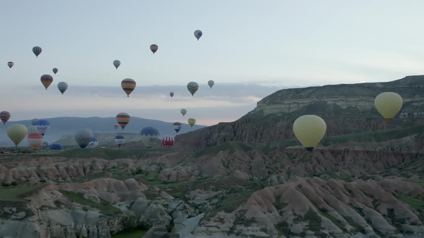 A large number of hot air balloons hover over a rocky terrain