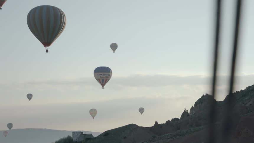Hot air balloons fly high over a mountainous terrain