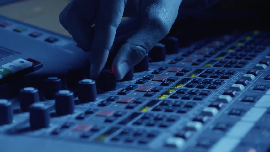 A person turns the dial on a sound board