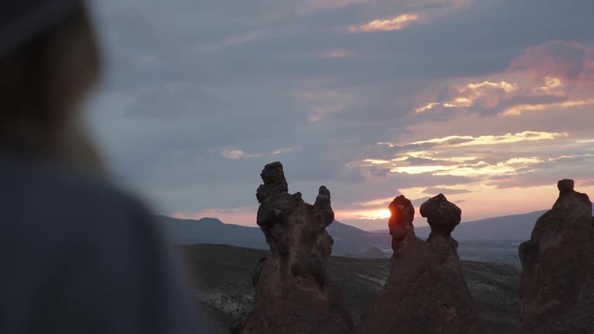 A young woman stands outdoors and looks over a group of unusual rock formation atop a hilltop