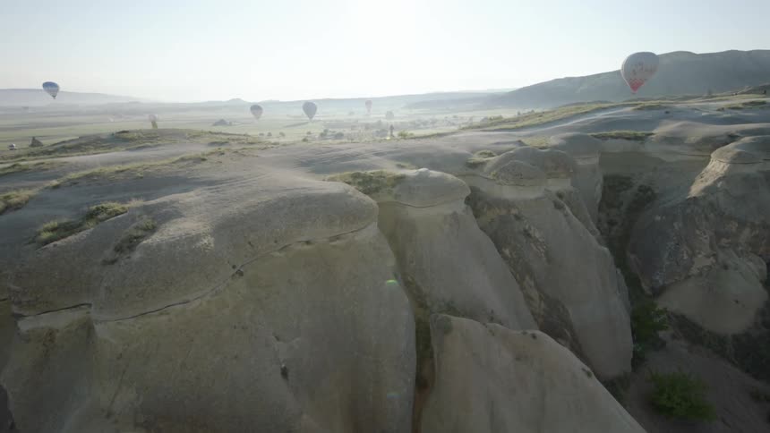 A rocky cliff with hot air balloons and the sky in the background