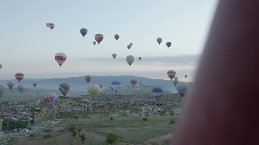 Many air balloons floating above the countryside just outside of a small town