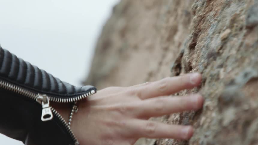 A persons fingers rubbing up against a rock