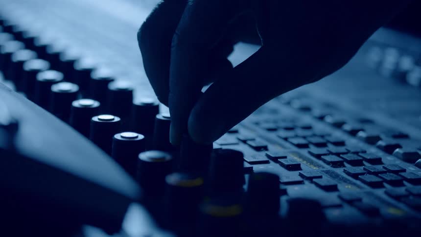 A persons hand adjusts a dial on a music control board in a blue light