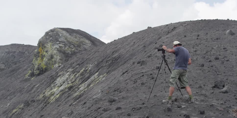 A man adjusts his camera on a rocky slope