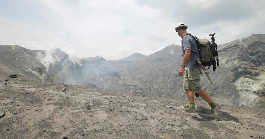A man hikes near a volcano with equipment strapped to his back