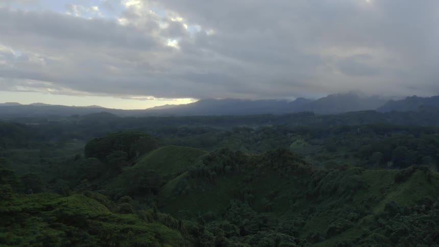 Thick forests cover a mountain range sitting beneath a cloudy sky