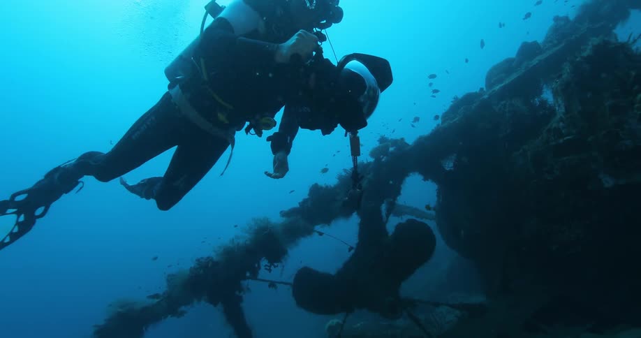 A scuba diver with photographic gear swims near an old wrecked plane