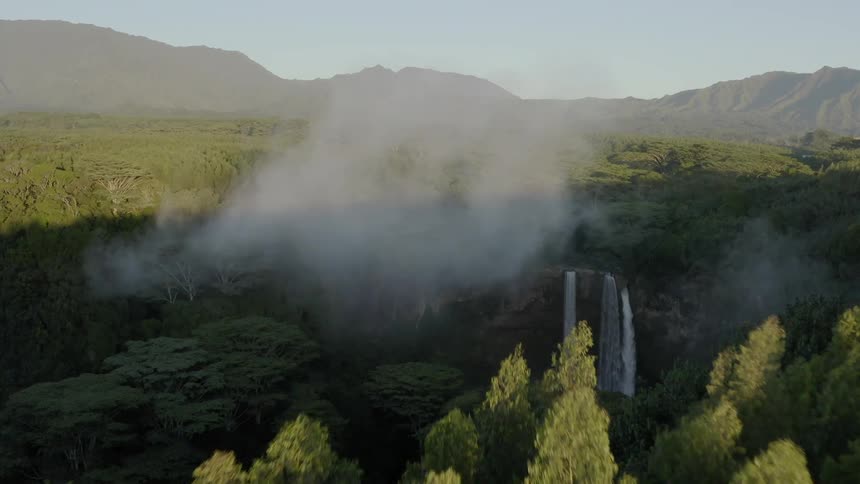 In the midst of a sprawling forest some small clouds of fog hangs above a rocky waterfall