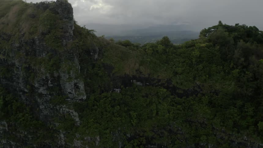Aerial footage flying over a tree covered mountain range that opens onto flat land dotted with buildings