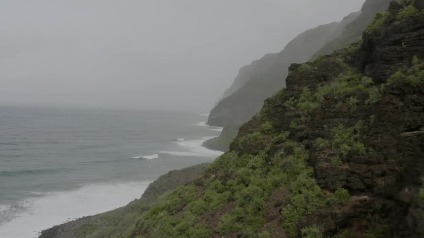 A mountain range and rocky cliffs covered in vegetation line the ocean shore line on an overcast day