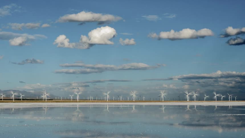 Wind turbines spin near the water under a blue sky