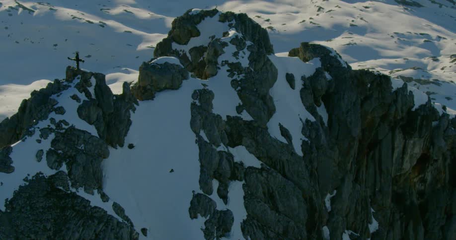 A cross stands on a ridge over a snow covered rocky slope