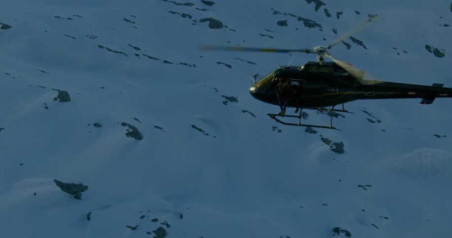 A helicopter flies over a snow covered rocky terrain
