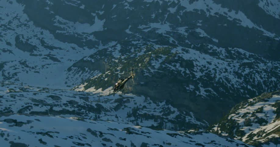 Helicopter flies over snow and forest covered mountain