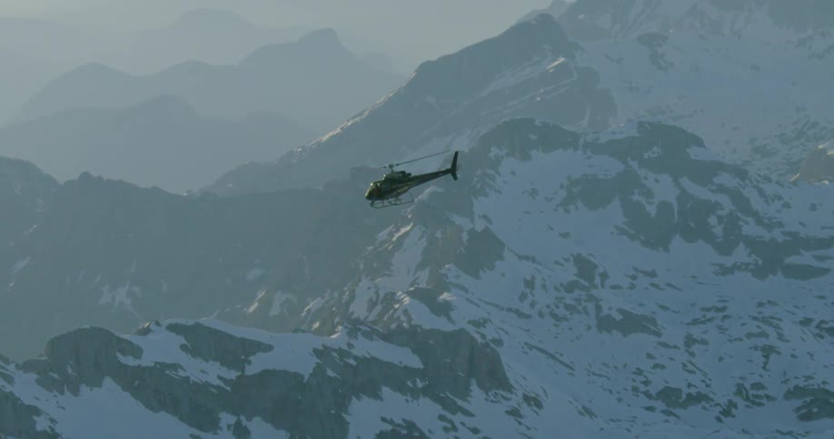 A helicopter is flying above mountains covered in snow
