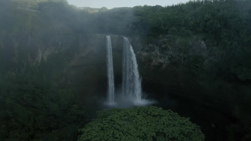Surrounded by forest a waterfall plunges over cliff into pool during foggy day