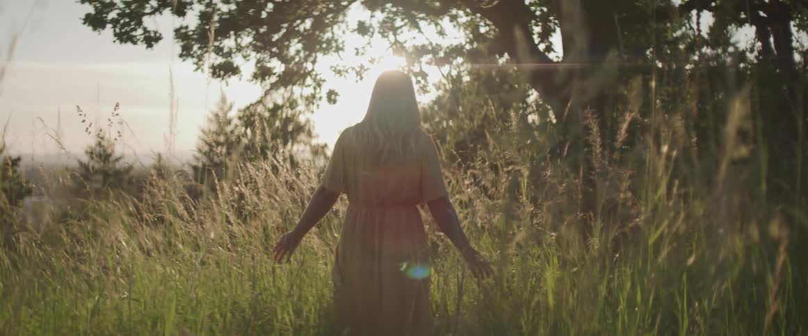 A female walking through tall grass towards a large tree