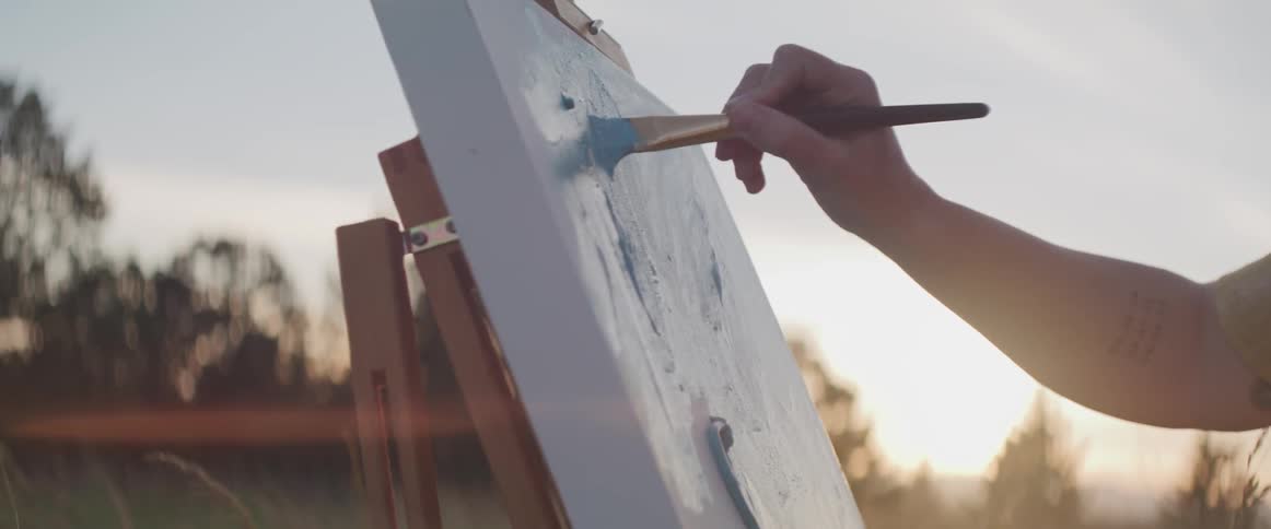 A person painting on a canvas while outdoors in the evening