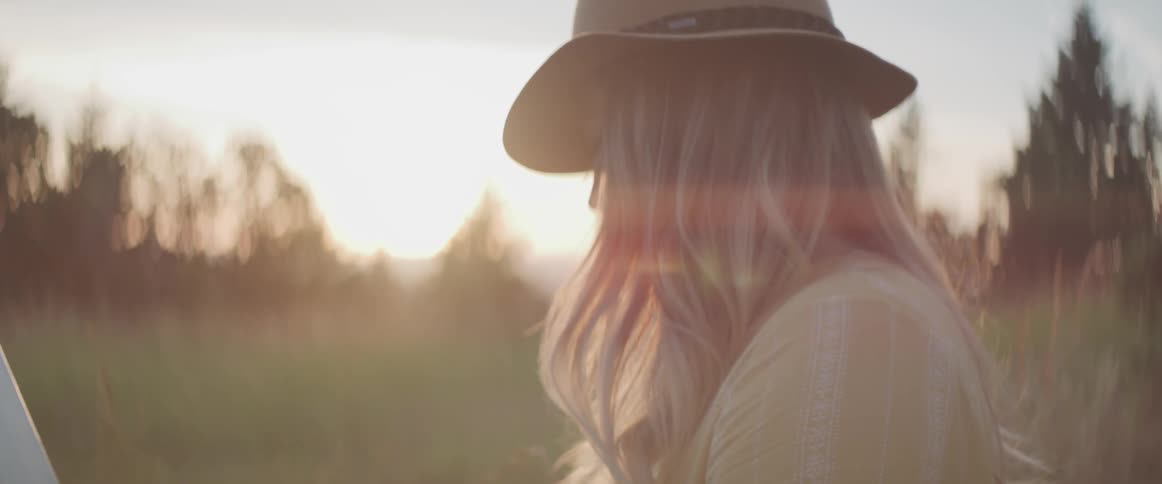 Woman paints outdoors in grassy field as sun rises
