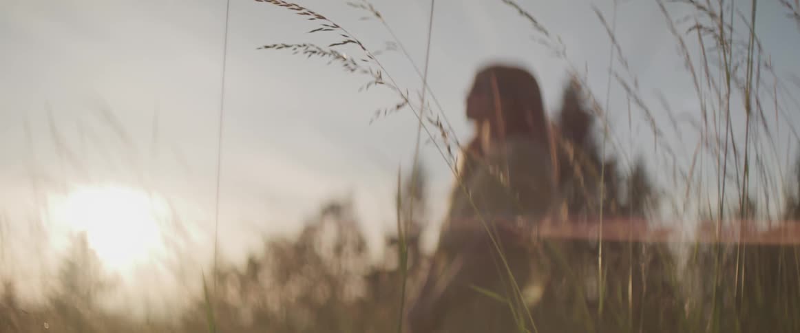 Woman stands in field with hands clasped as sun rises on horizon