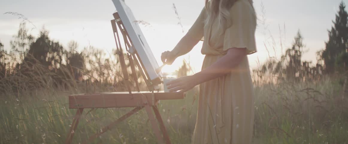 A woman paints on a canvas outside in a grass field
