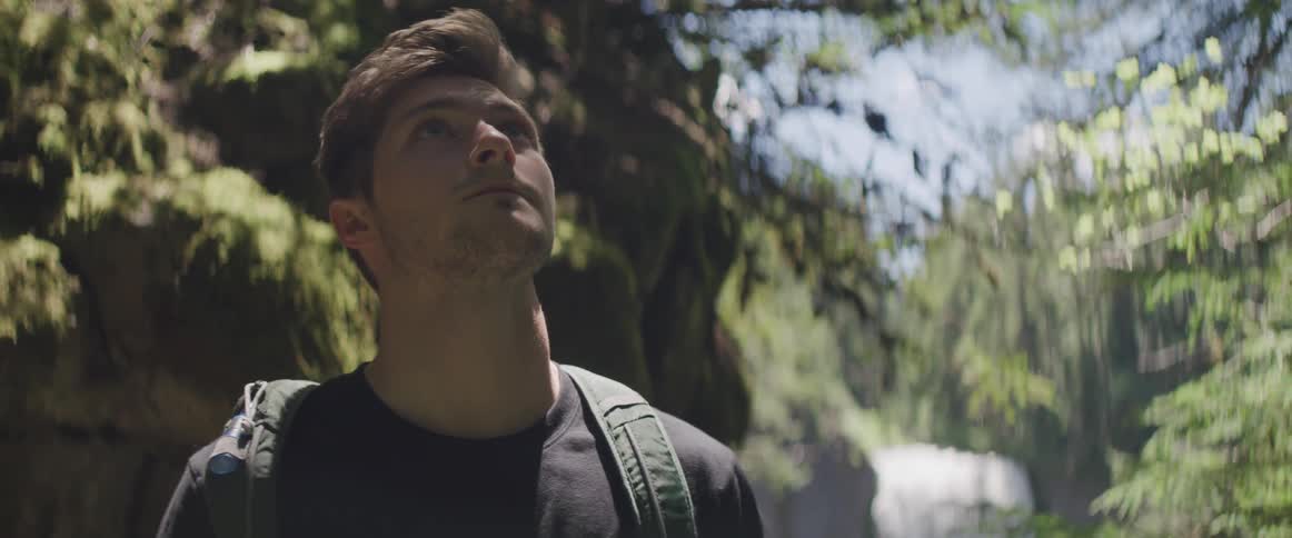 Man stands outdoors looking up with low waterfall in background