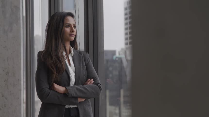 A woman in a suit standing near the window of a skyscraper looking outdoors