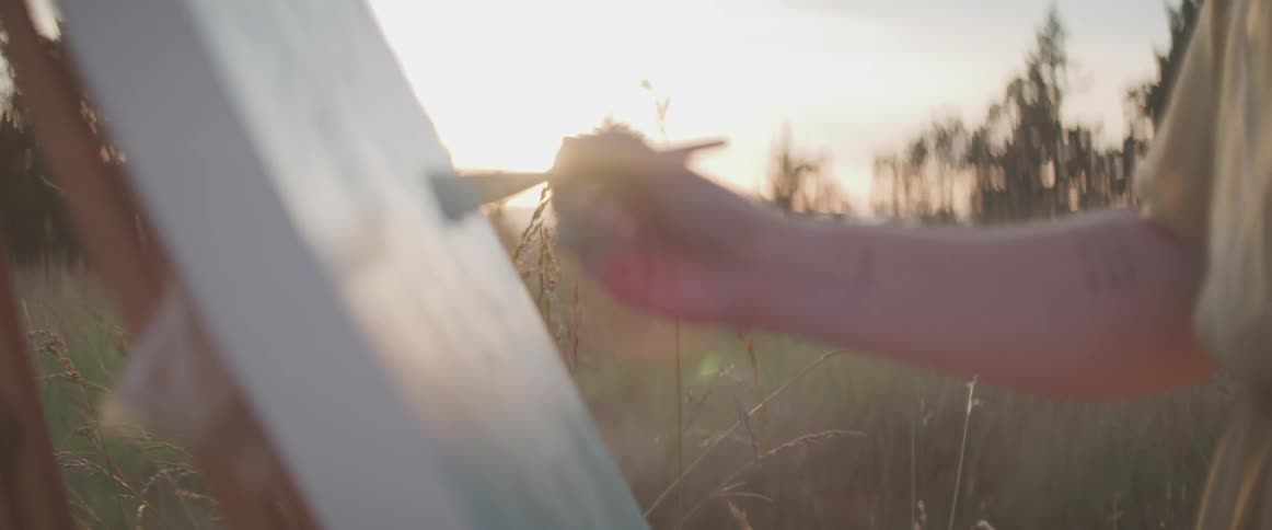 Woman painting art outdoors in a field near sunset