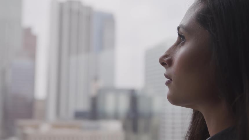 A woman looks out a window at a large city
