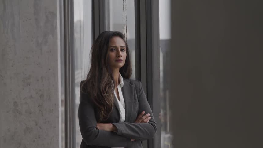 Woman stands in front of a window with her arms crossed as she turns her head to her right