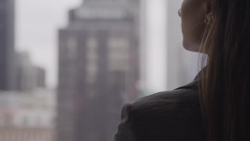 A woman stands at a window and looks out at the city outside