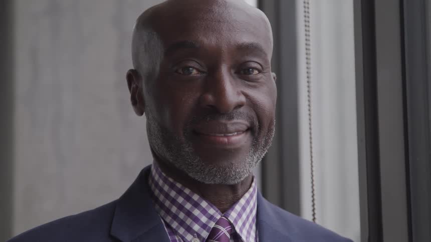 A black man turns his head and looks ahead and smiles