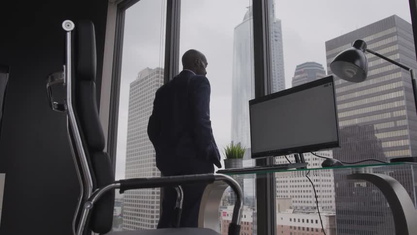 Man in a suit stands looking out of an office window