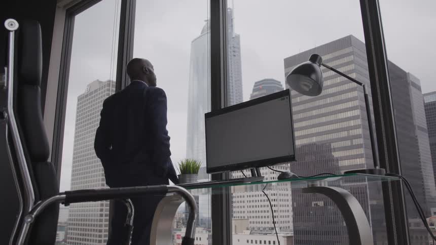 A man looks out of his office window with a view of skyscrapers and high rise buildings