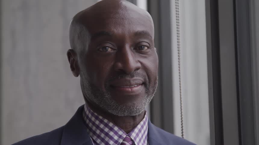 Bald headed black man looks at the camera smilingly in the office