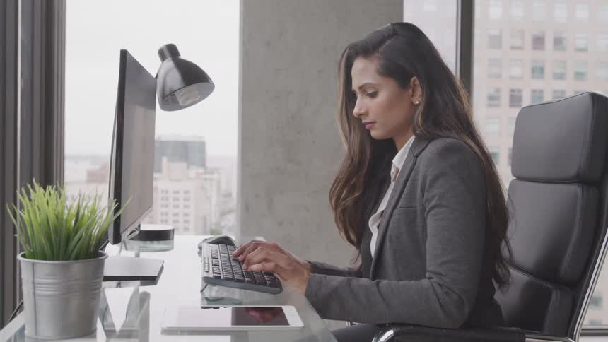 Businesswoman sitting at the glass table uses computer in the office