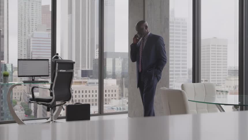 A man in a corner office walking and talking on his smart phone