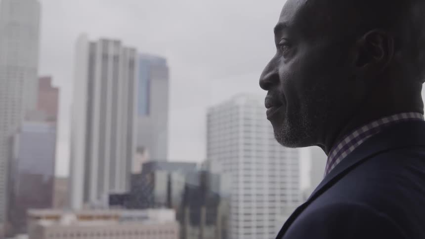 Black business man looking out of office window to the city