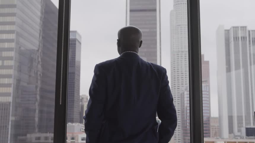 Businessman standing at his office window looking at the downtown area with his hands in his pockets